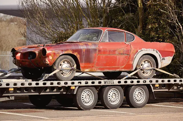 Coupé ancien rouge arrimé sur un plateau porte-voiture
